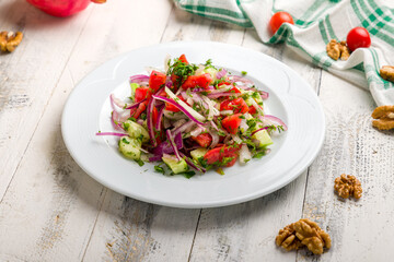Vegetable salad with tomatoes and cucumbers and red onion on white wooden table