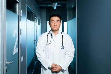 Portrait of a serious Asian doctor, a man in the clinic, in the corridor near the wards, staring intently at the camera