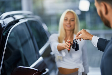 Fototapeta Cheerful caucasian woman taking keys from her new car while standing with male consultant at modern salon. Concept of people, purchase and selling. obraz