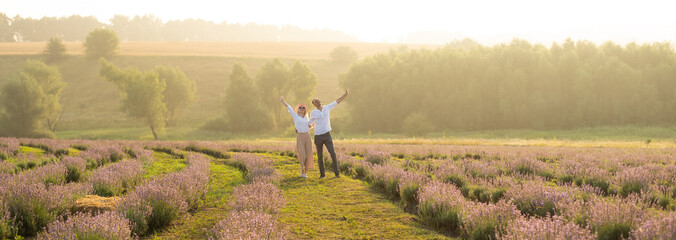 Smiling young couple embracing at the lavender field, holding hands, walking.