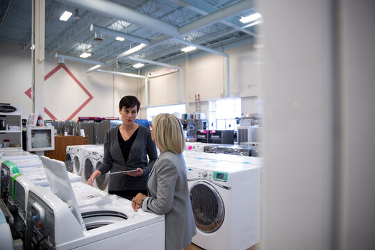 Saleswoman with digital tablet helping senior woman shopping for clothes washer in appliance store