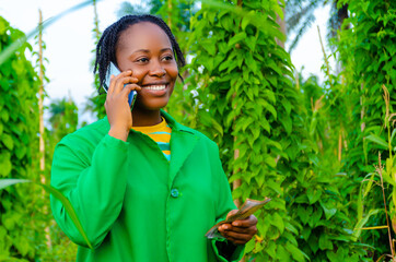 pretty african woman in the farm making calls in the farm while holding money on her other hand