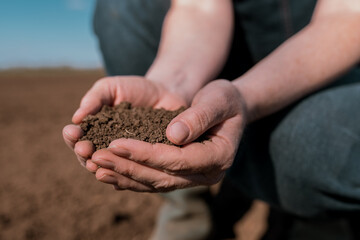Hands of female farmer full of freshly ploughed fertile soil ground