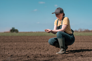 Female farmer agronomist checking the quality of ploughed field soil before sowing season - obrazy, fototapety, plakaty