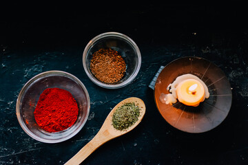 spices and herbs on spoons burning candle on black background