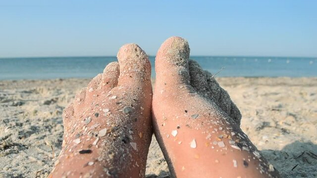 Two bare feet of caucasian woman soiled in sand with shell rock on sandy sea shore on sunny summer day close-up. Relaxing on sea sandy beach. Concept of rest, relaxation, vacation, travel tourism
