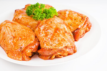 Raw marinated in red sauce chicken thighs on a white plate, on a white isolated background. Top of view.Isolated object, copy space.Raw chicken marinated. Chicken semi-cooked thighs.