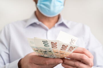 Counting small Cash banknotes of Czech Republic Koruna. Finance during coronavirus in Czechia concept. CZK small banknotes. Man in a protective medical face mask holds krona cash.