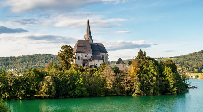 Sunlit church in the village of Maria Worth on the shores of Lake Worthersee in the Austrian mountains. Lake with clear clear water.