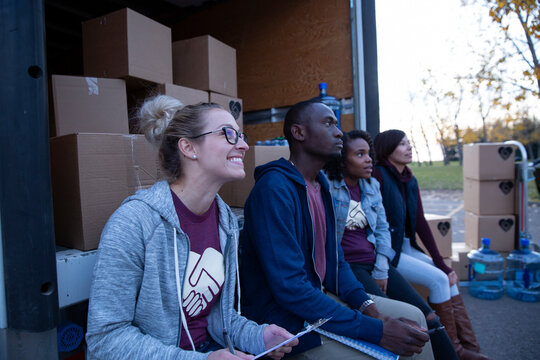 Smiling volunteers sitting at back of truck with cardboard boxes