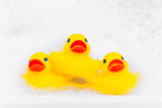 Pyramid of three yellow rubber duck for bathing in the bathroom among relaxing bubble baths, front view, copy space for advertising text. Home spa procedures.