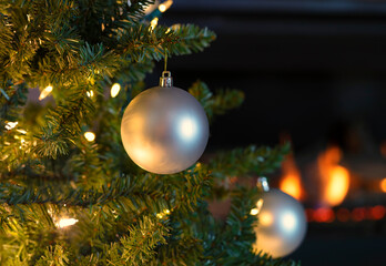 Single silver ball ornament hanging from Christmas tree with glowing fireplace in background - 478645190