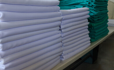 Stack of white sheets and green surgical cloths in an industrial laundry.