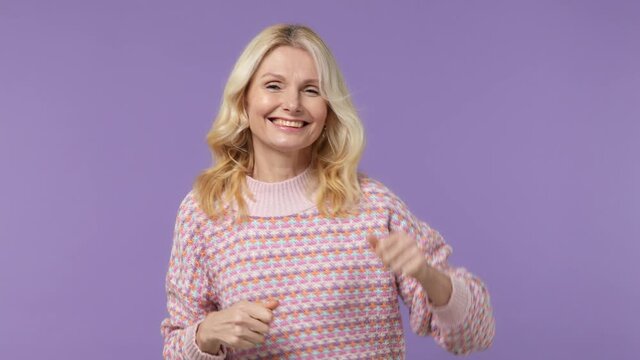 Vivid cheerful elderly blonde woman lady 40s years old wears warm shirt dance clench fists waving rising hands have fun enjoy celebrate isolated on plain pastel light purple background studio portrait