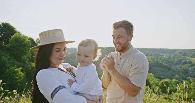 Mother and father dance and sing with amusing baby in meadow