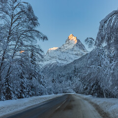 Winter paved road through the forest leading to high mountains.
