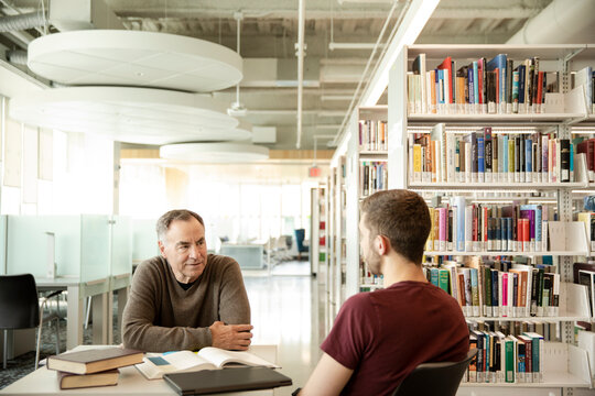 Senior man talking to university student in library