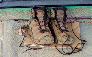 Mud covered well worn hiking boots with untied laces on a porch