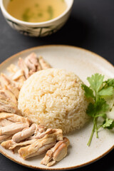 Hainanese chicken rice with coriander, cucumber and chicken soup on black background. Local food in East and Southeast Asia