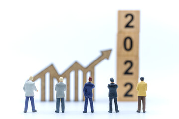 2022 New Year and Business Planning Concept. Closeup of group of businessman miniature figures standing and looking to wooden arrow chart sign and stack of wooden number block on white background.