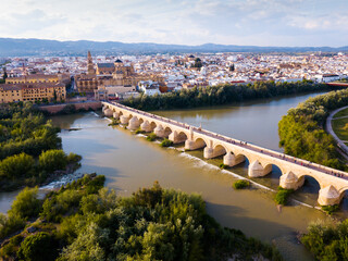 Fototapeta na wymiar Scenic aerial view of ancient Roman bridge across Guadalquivir river and Moorish architecture of Mezquita-Catedral on background with Cordoba cityscape, Spain