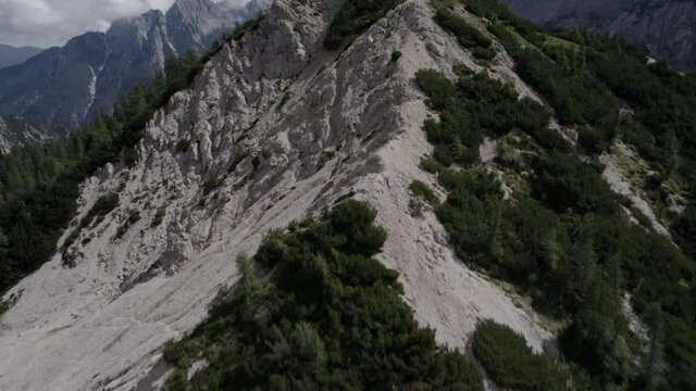 Drone video with an ascending frontal descriptive plane over the Vrsc pass in Slovenia with hiker at the top ascending walking and a horizon with mountains.