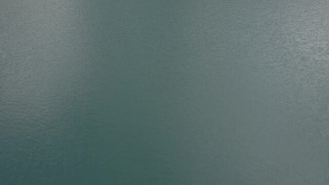 Drone video with descriptive side reverse plane over Braies lake with boats with people rowing and mountains on the horizon.