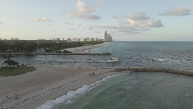 Ships motoring below, paramotor flies over Miami beach channel inlet