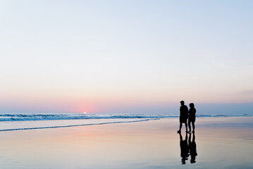 Silhouette of unrecognizable couple walking on the beach during sunset while holding hands