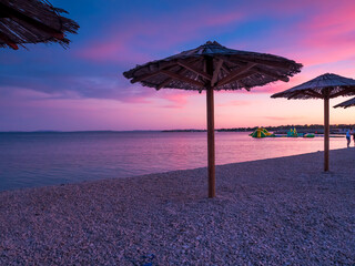 View of the beautiful blue and purple sunset, sky and straw beach umbrellas