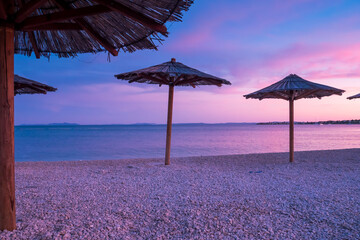 View of the beautiful blue and purple sunset, sky and straw beach umbrellas
