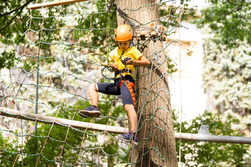 Happy child climbing in the trees. Rope park. Climber child. Early childhood development. Roping park. Balance beam and rope bridges. Rope park - climbing center