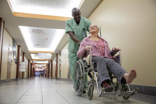Male nurse pushing female patient in wheelchair down hospital corridor