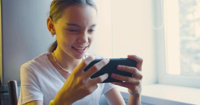 Teenager girl playing video game touching smartphone screen - she having fun at home.