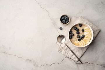 Oatmeal. Porridge with bananas and blueberries for healthy breakfast or lunch. Flat lay on linen napkin and concrete background