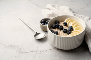 Oatmeal. Porridge with bananas and blueberries for healthy breakfast or lunch on linen napkin and concrete background
