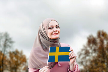 Muslim woman in hijab holds flag of Sweden