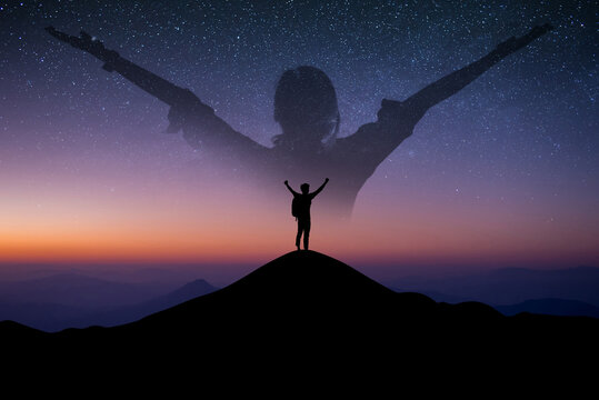 Silhouette of young traveler standing alone on top of the mountain with double exposure young man standing and open arm and feel free over the sky with star and Milky Way  in summer season.