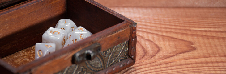 Set of role playing white dices lie in storage box on gaming table made of wood, banner: concept...