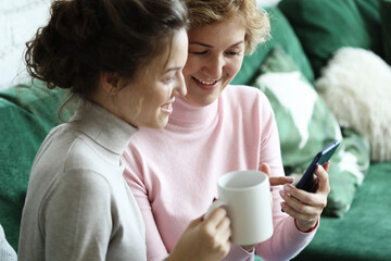 Aged woman and her adult daughter using smartphone at home.