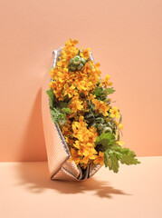 Cosmetic bag silver color with bright yellow flowers and green leaves on pastel orange background. Luxurious gift set.