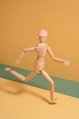 Athletic wooden man fast run with headband pink color. Body shadow falls on yellow-green background. Aesthetic of dynamic sport movement.