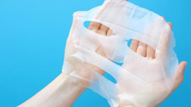 Female hands hold sheet of facial mask on blue background.