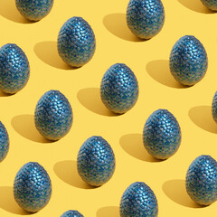 Pattern made with blue shiny eggs on yellow background. Positive mood, happiness and festive inspiration.