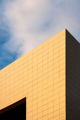 Golden sunlight on surface of modern office building wall against white clouds with blue sky at morning time in perspective view and vertical frame