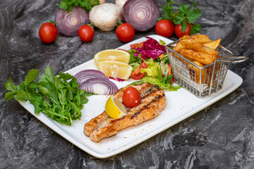 Grilled salmon with salad and french fries on a white plate