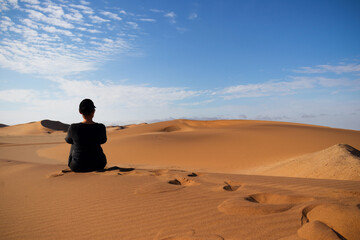 Fototapeta na wymiar A woman is sitting on the golden sand dune of the Namib desert.