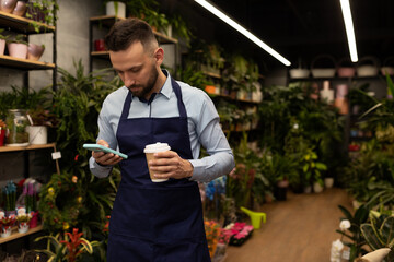 man florist businessman with a phone in his hand and a cup of coffee in a flower and bouquet shop