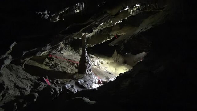 Unseen caver lights calcite column in muddy underground cave chamber