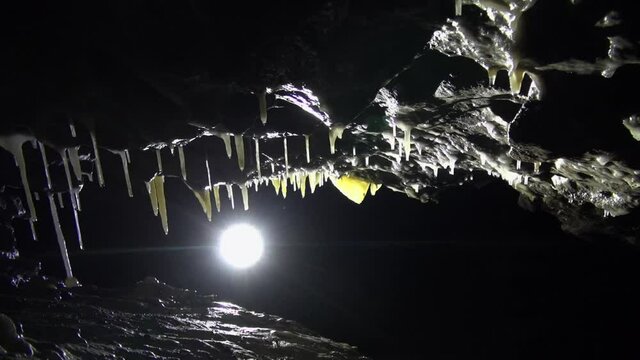 Backlit slanted ceiling with speleothems in dark black cave passage